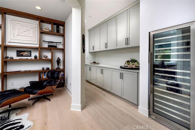 bar with gray cabinetry, light hardwood / wood-style floors, and beverage cooler