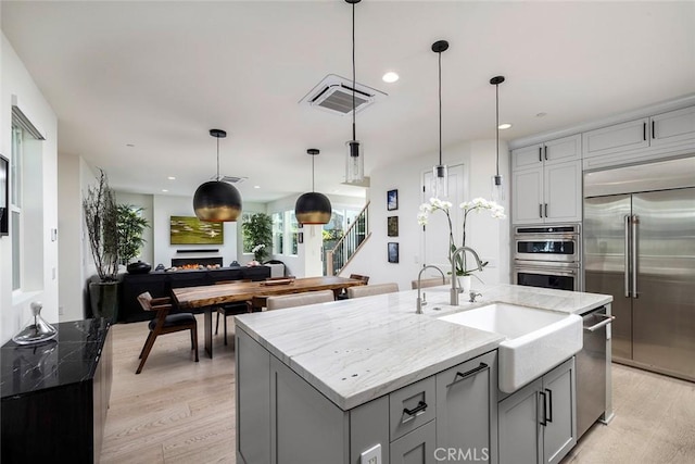 kitchen featuring light stone countertops, decorative light fixtures, appliances with stainless steel finishes, and a center island with sink