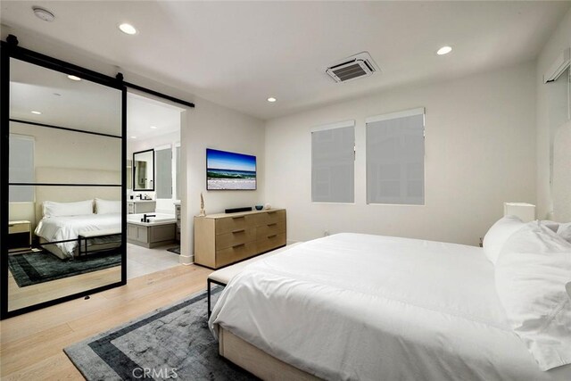 bedroom featuring a barn door, connected bathroom, and light hardwood / wood-style flooring