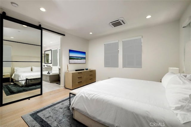 bedroom featuring ensuite bathroom, light hardwood / wood-style flooring, and a barn door