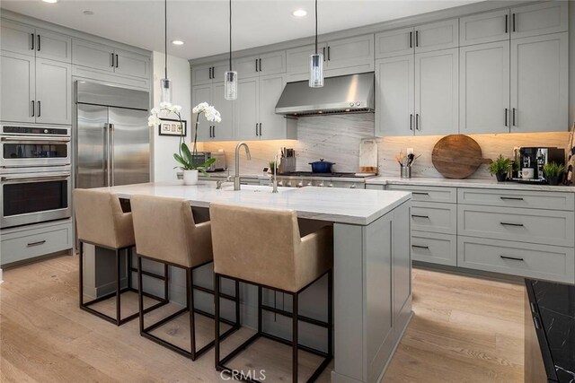 kitchen featuring extractor fan, an island with sink, appliances with stainless steel finishes, decorative backsplash, and sink