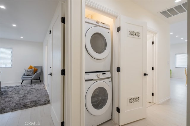 laundry room with stacked washer and dryer and light hardwood / wood-style flooring