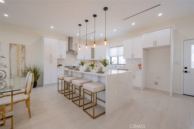 kitchen featuring a center island, wall chimney exhaust hood, decorative light fixtures, white cabinetry, and tasteful backsplash