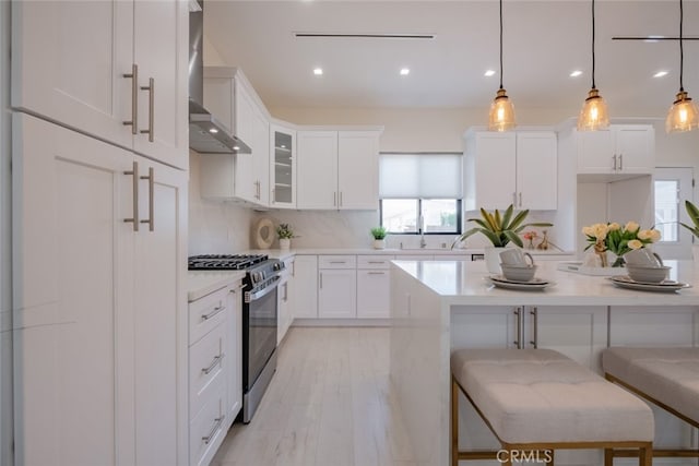 kitchen featuring white cabinetry, stainless steel range with gas cooktop, hanging light fixtures, and a breakfast bar area