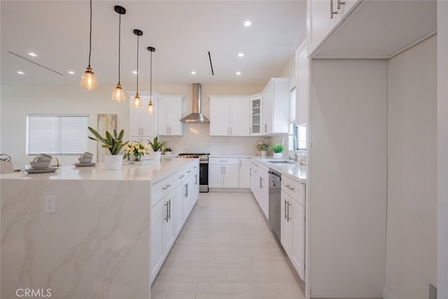 kitchen with hanging light fixtures, appliances with stainless steel finishes, wall chimney range hood, and white cabinetry