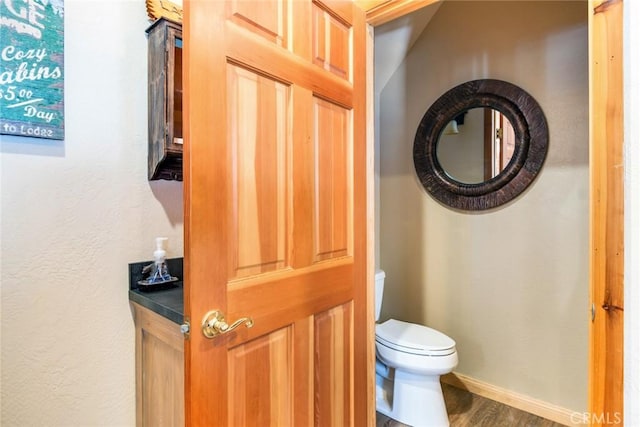 half bathroom featuring toilet, baseboards, and wood finished floors