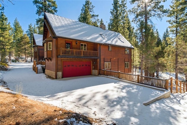 snow covered property with a garage, stone siding, faux log siding, and a chimney