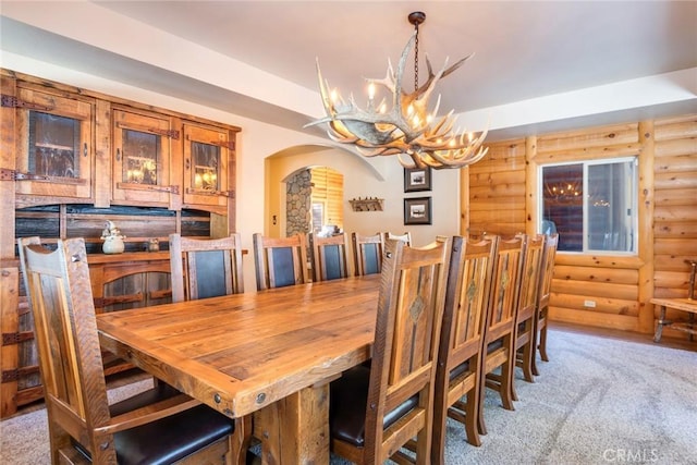 dining room featuring arched walkways, rustic walls, a chandelier, and light colored carpet