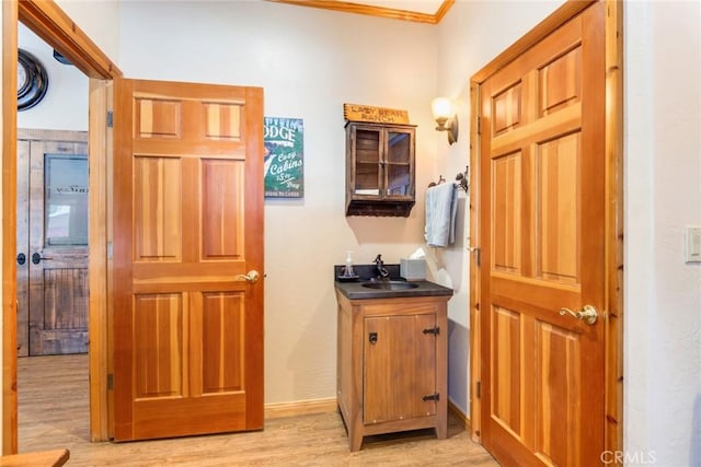 hallway with baseboards, light wood-type flooring, a sink, and crown molding