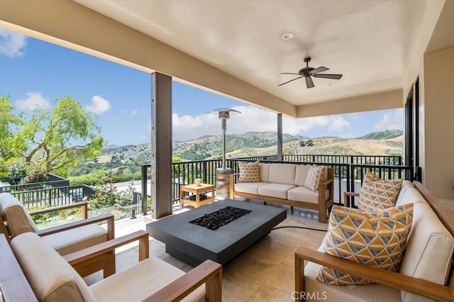 view of patio with ceiling fan, an outdoor living space with a fire pit, and a mountain view