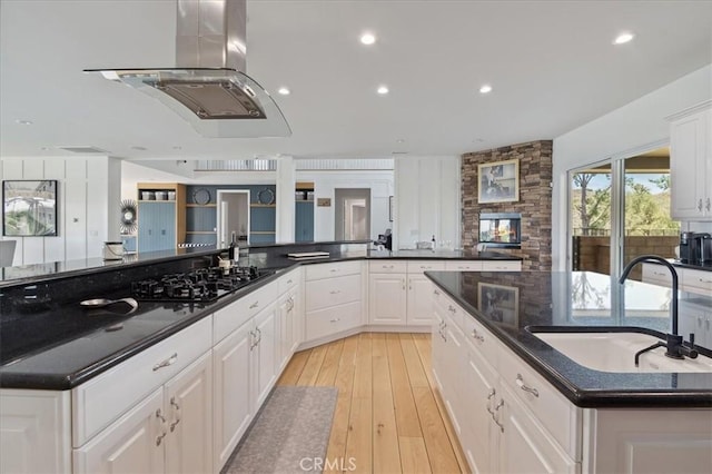 kitchen featuring white cabinets, black gas stovetop, island exhaust hood, sink, and light hardwood / wood-style flooring