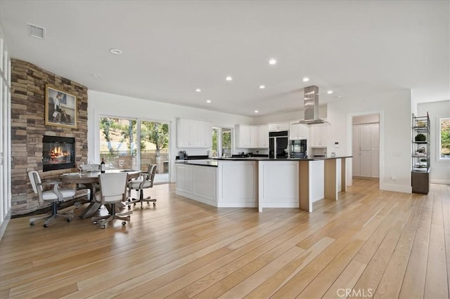 kitchen with a fireplace, a center island, light hardwood / wood-style flooring, white cabinets, and island range hood