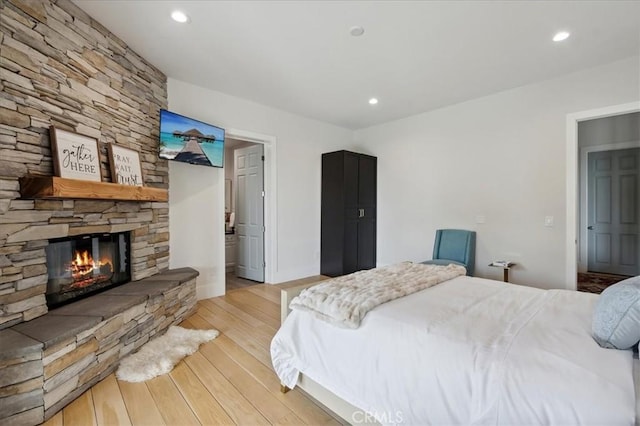 bedroom featuring a stone fireplace and light hardwood / wood-style floors