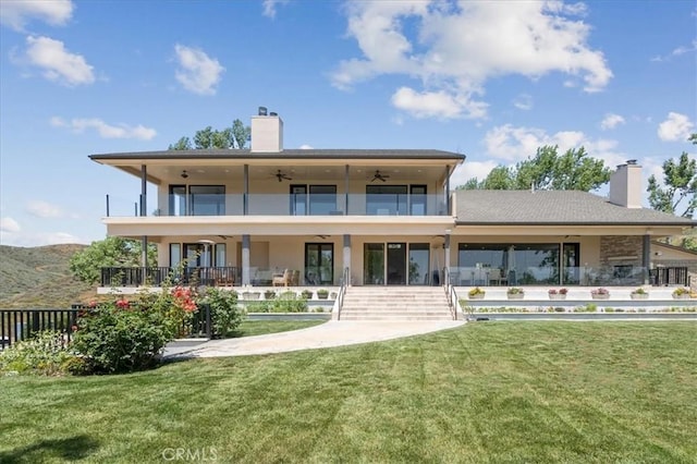 rear view of property with a balcony, a yard, and ceiling fan