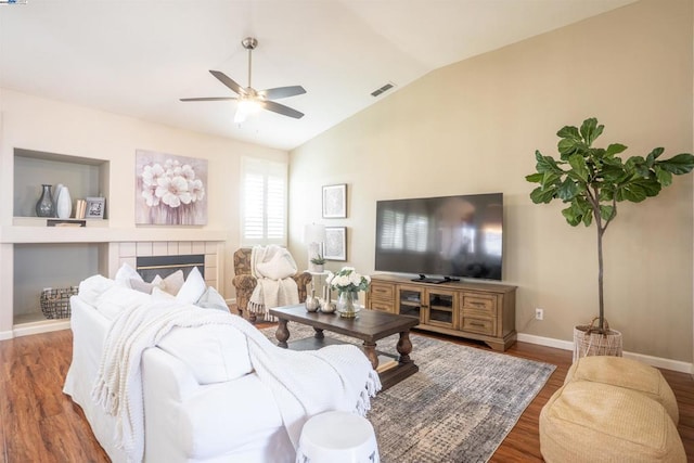 living room with lofted ceiling, ceiling fan, dark wood-type flooring, and a tiled fireplace