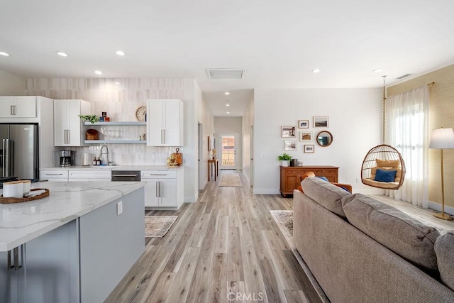 kitchen with decorative light fixtures, high end refrigerator, sink, light stone countertops, and white cabinets