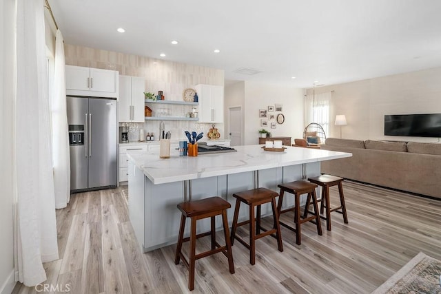 kitchen with white cabinets, light hardwood / wood-style floors, a kitchen breakfast bar, a large island, and high end fridge