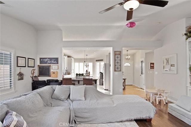 living room featuring ceiling fan with notable chandelier, light hardwood / wood-style flooring, and lofted ceiling