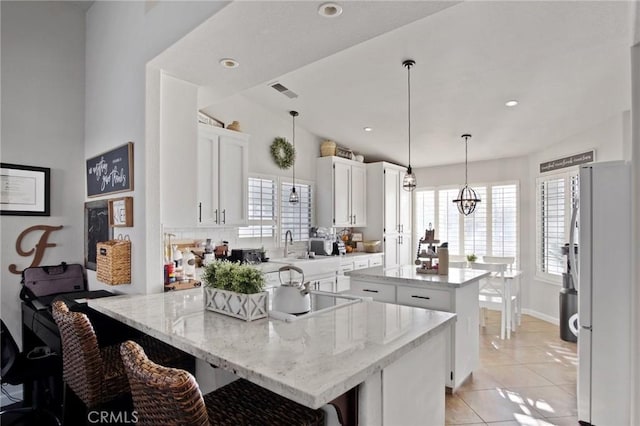 kitchen with white cabinets, a center island, white fridge, light stone counters, and light tile patterned floors