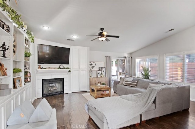 living room with ceiling fan, vaulted ceiling, dark wood-type flooring, and a tile fireplace