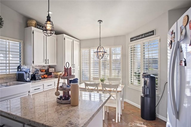 kitchen with white cabinets, decorative light fixtures, white refrigerator, an inviting chandelier, and light stone counters