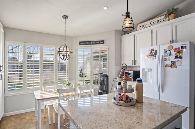 kitchen with light stone counters, white fridge with ice dispenser, white cabinets, and hanging light fixtures