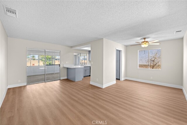 unfurnished living room with a textured ceiling, ceiling fan, and light wood-type flooring