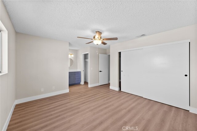 unfurnished bedroom with ensuite bathroom, ceiling fan, a closet, a textured ceiling, and light hardwood / wood-style flooring