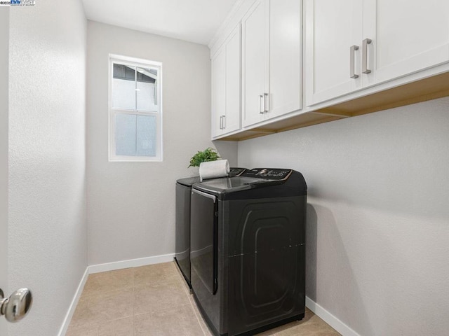 clothes washing area featuring light tile patterned floors, washer and dryer, and cabinets