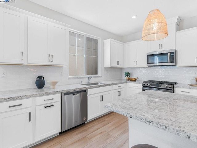 kitchen with stainless steel appliances, backsplash, hanging light fixtures, white cabinets, and sink