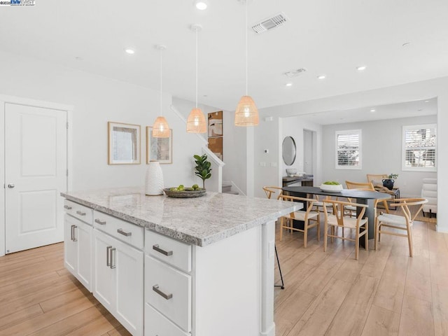 kitchen featuring white cabinetry, light hardwood / wood-style floors, a kitchen island, and decorative light fixtures