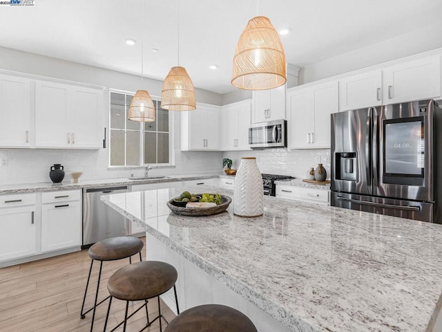 kitchen featuring a kitchen island, pendant lighting, stainless steel appliances, and white cabinetry