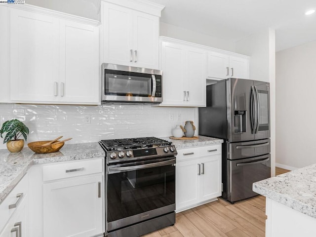 kitchen with light wood-type flooring, white cabinets, decorative backsplash, and stainless steel appliances