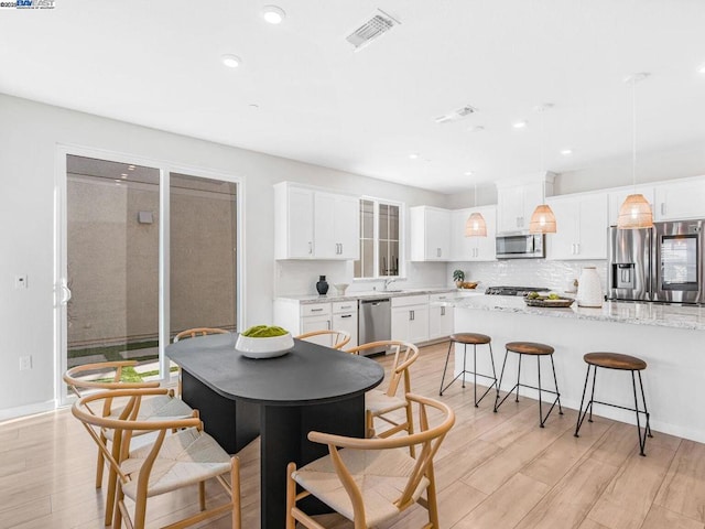 kitchen featuring backsplash, hanging light fixtures, appliances with stainless steel finishes, white cabinets, and light stone counters