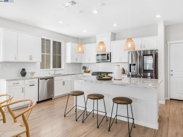 kitchen with white cabinetry, decorative light fixtures, a kitchen island, and appliances with stainless steel finishes