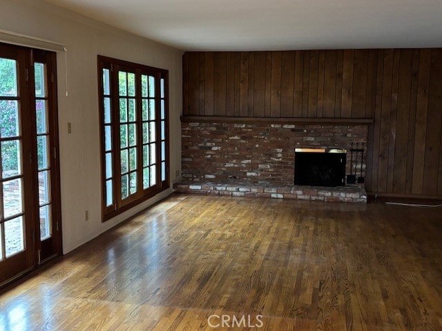 unfurnished living room featuring a healthy amount of sunlight, a brick fireplace, wood walls, and hardwood / wood-style floors