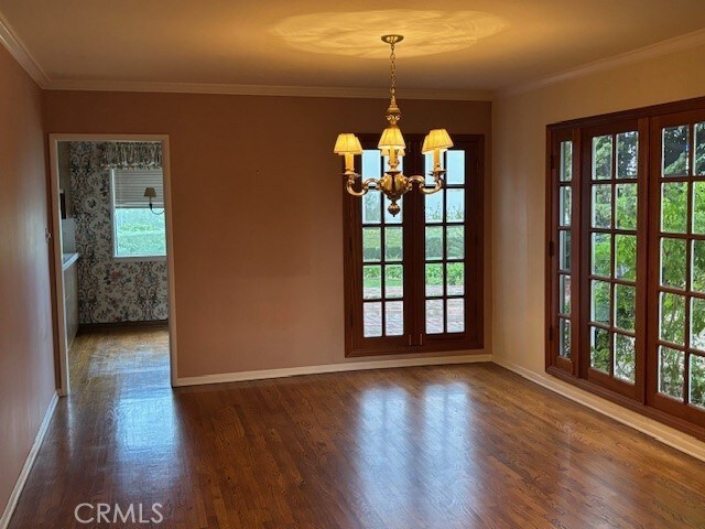 unfurnished dining area featuring an inviting chandelier, crown molding, dark hardwood / wood-style floors, and a healthy amount of sunlight