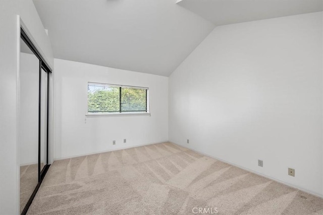 unfurnished bedroom featuring light carpet, a closet, and lofted ceiling