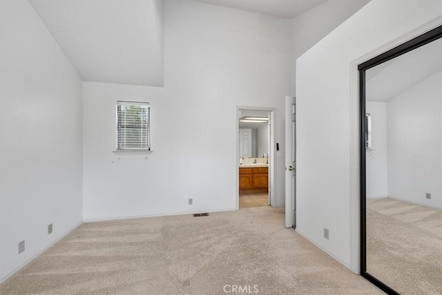 unfurnished bedroom featuring high vaulted ceiling, connected bathroom, and light carpet