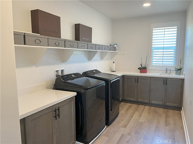 laundry area with light wood-type flooring, independent washer and dryer, a sink, and cabinet space