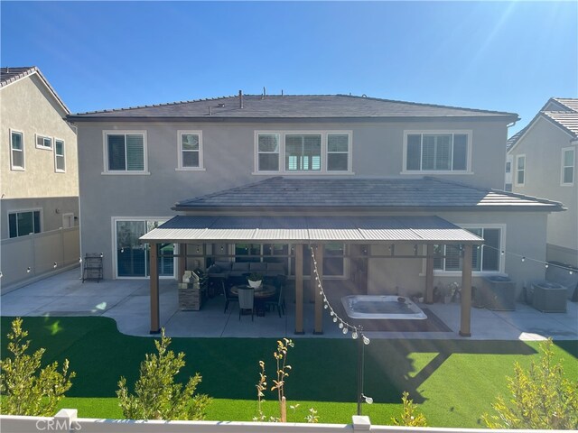 back of house featuring a yard, a hot tub, and a patio