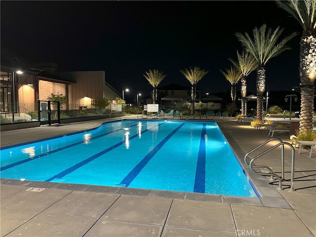 pool at twilight with a patio area, fence, and a community pool