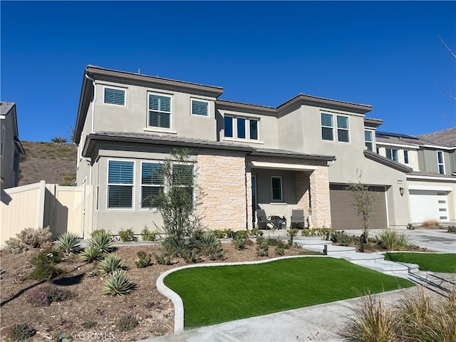 prairie-style home with stucco siding, concrete driveway, fence, a garage, and stone siding