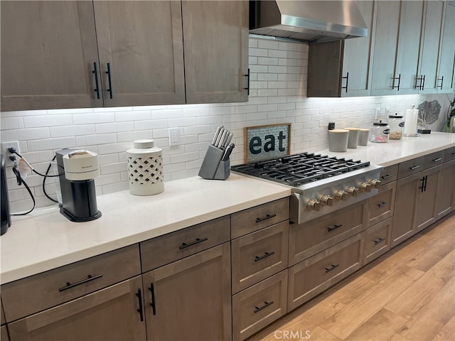 kitchen featuring stainless steel gas cooktop, tasteful backsplash, light countertops, light wood-style floors, and wall chimney range hood