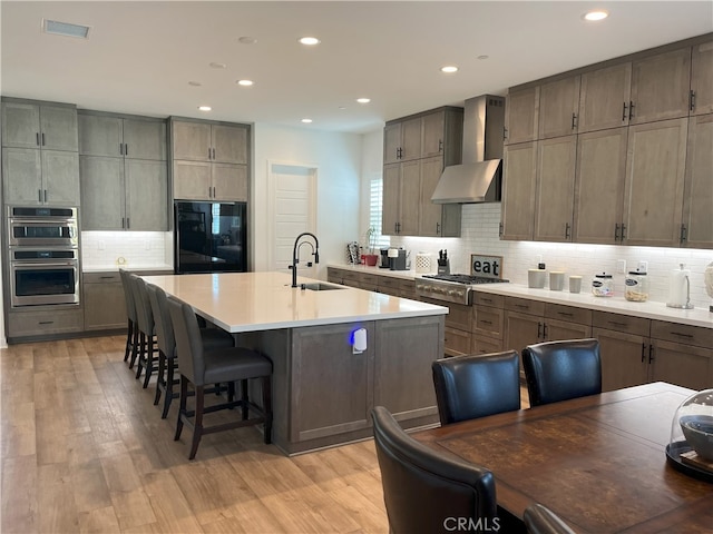 kitchen with wall chimney exhaust hood, light wood-style floors, a sink, and stainless steel appliances