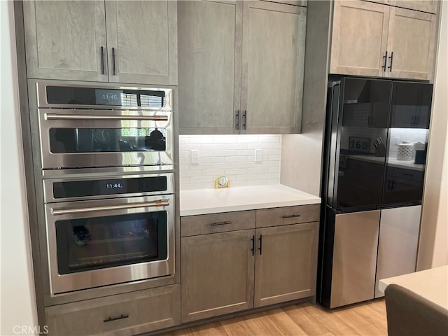 kitchen featuring black fridge, backsplash, light wood-type flooring, and stainless steel double oven