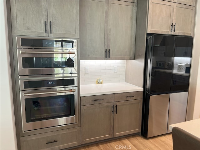 kitchen featuring stainless steel appliances, light wood-type flooring, light countertops, and decorative backsplash