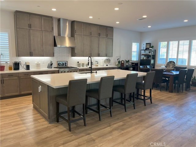 kitchen with wall chimney exhaust hood, light wood-style flooring, a sink, and light countertops