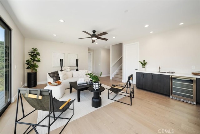 living room featuring wine cooler, ceiling fan, sink, and light hardwood / wood-style flooring