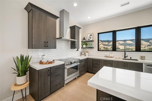 kitchen featuring sink, dark brown cabinetry, wall chimney range hood, and stainless steel stove